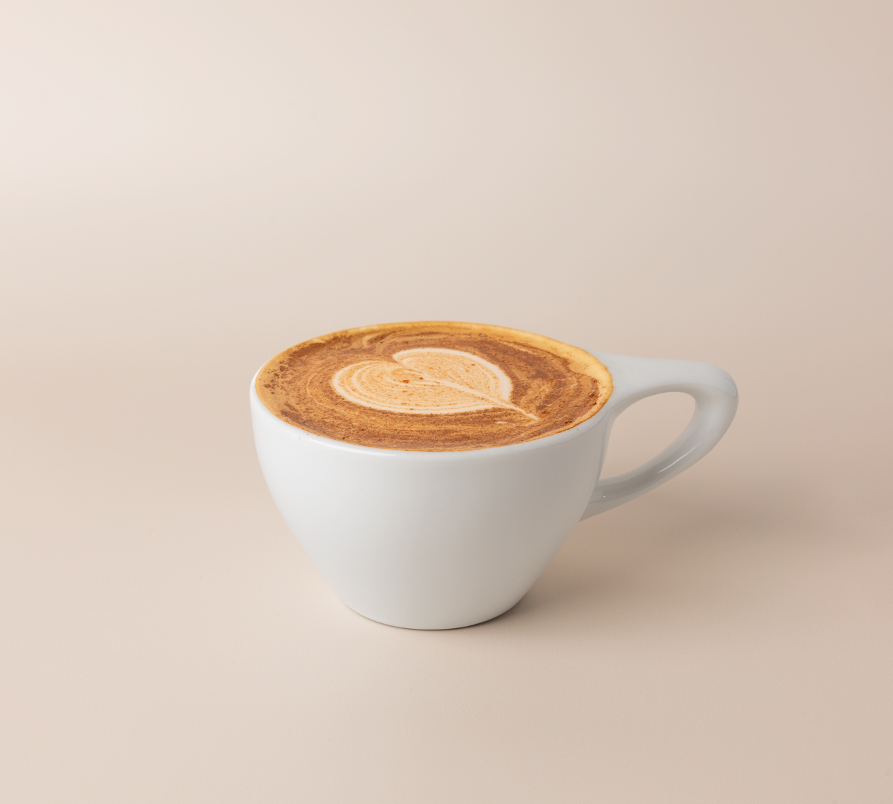 Apple cider donut latte in a white ceramic cup, heart latte art dusted with ground cinnamon, warm cream background.