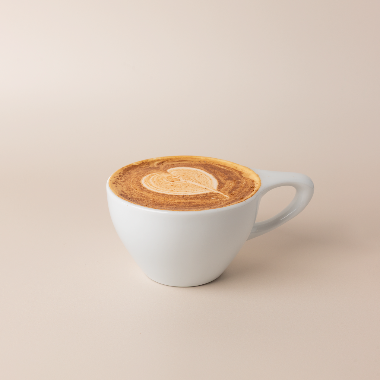Apple cider donut latte in a white ceramic cup, heart latte art dusted with ground cinnamon, warm cream background.