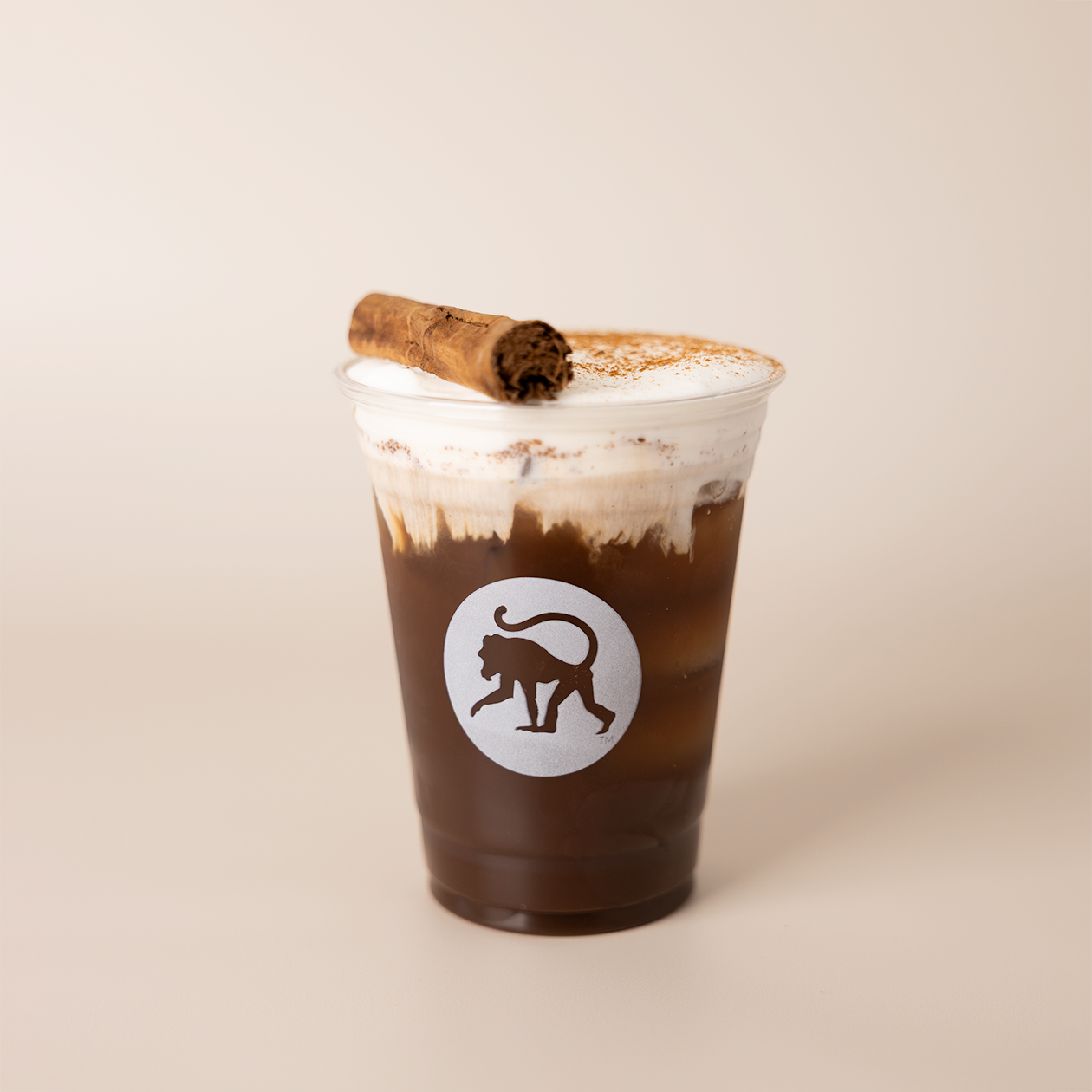 Campfire cold brew in a Frothy Monkey branded cup, topped with cold foam, a cocoa dusting, and a cinnamon stick.