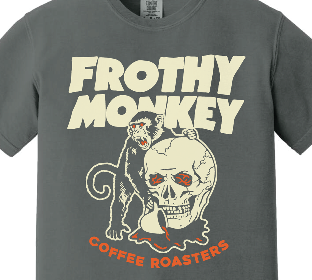 Frothy Monkey Coffee Roasters skull T-shirt, a red-eyed monkey climbing a cracked skull and holding a coffee cup, cream and orange print on a Pepper Comfort Colors shirt