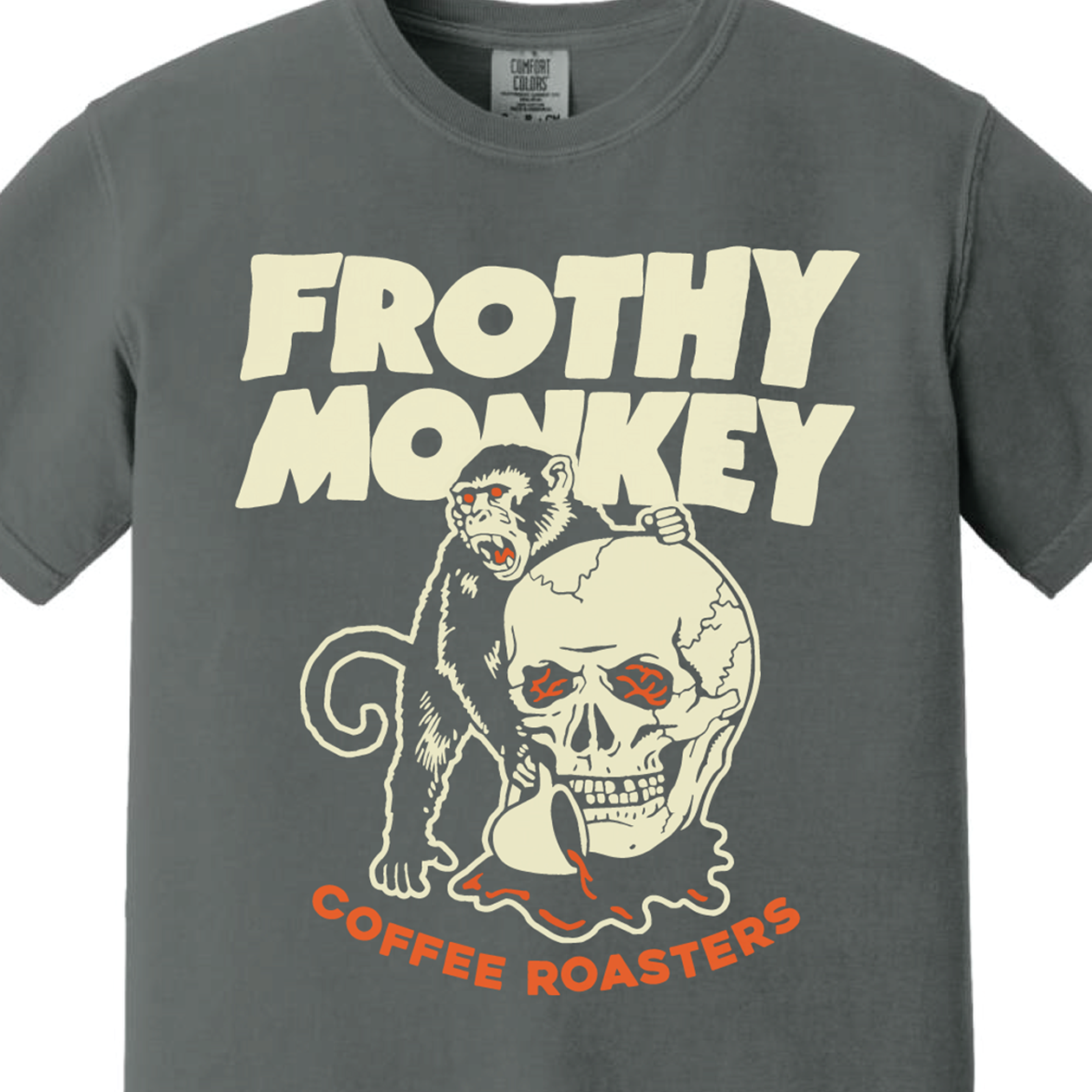 Frothy Monkey Coffee Roasters skull T-shirt, a red-eyed monkey climbing a cracked skull and holding a coffee cup, cream and orange print on a Pepper Comfort Colors shirt