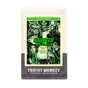 Haunted Howler 12oz bag from Frothy Monkey Coffee Roasters with a green 80s horror poster label by Neal Russler showing a werewolf, a witch at a cauldron, and a castle in a lightning storm