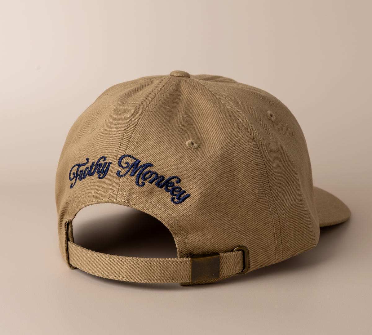 Back of the driftwood brown Frothy Monkey Kong dad hat showing the Frothy Monkey script logo embroidered in navy across the rear panels and the matching cotton adjustable strap with brass clasp