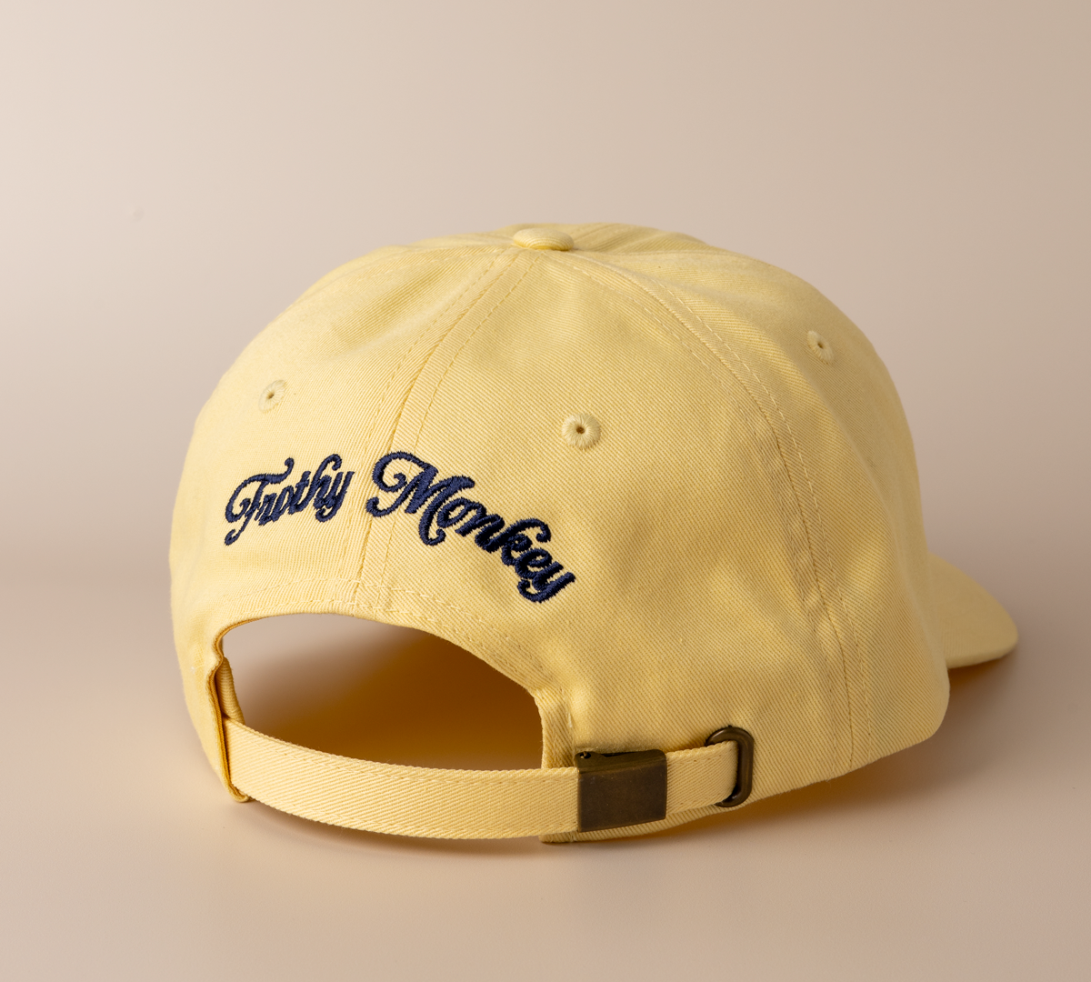 Back of the banana yellow Frothy Monkey Kong dad hat showing the Frothy Monkey script logo embroidered in navy across the rear panels and the matching cotton adjustable strap with brass clasp