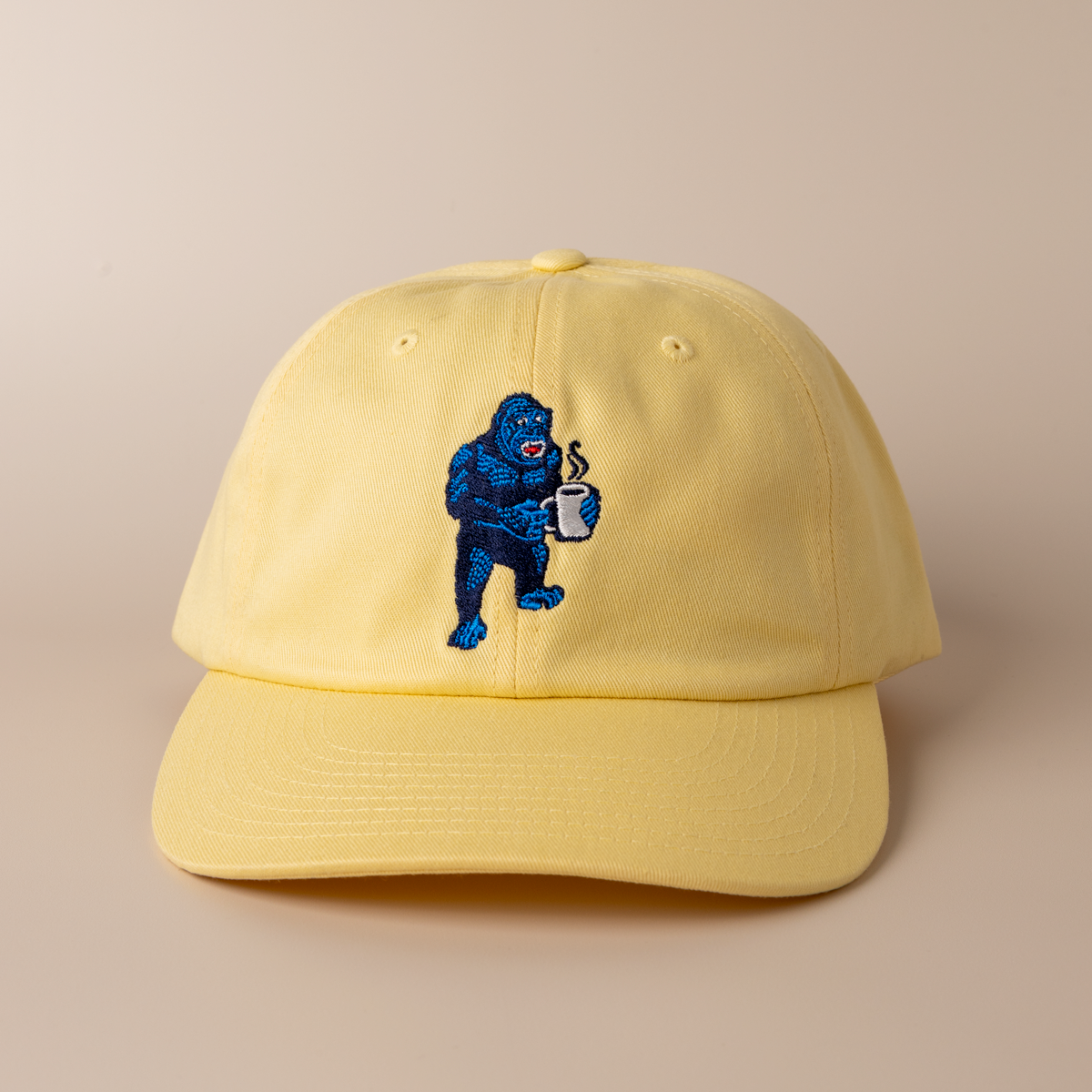 Frothy Monkey Kong dad hat in banana yellow with Kong the gorilla holding a steaming coffee mug embroidered on the front crown in navy and blue thread, unstructured six-panel premium cotton cap with pre-curved visor