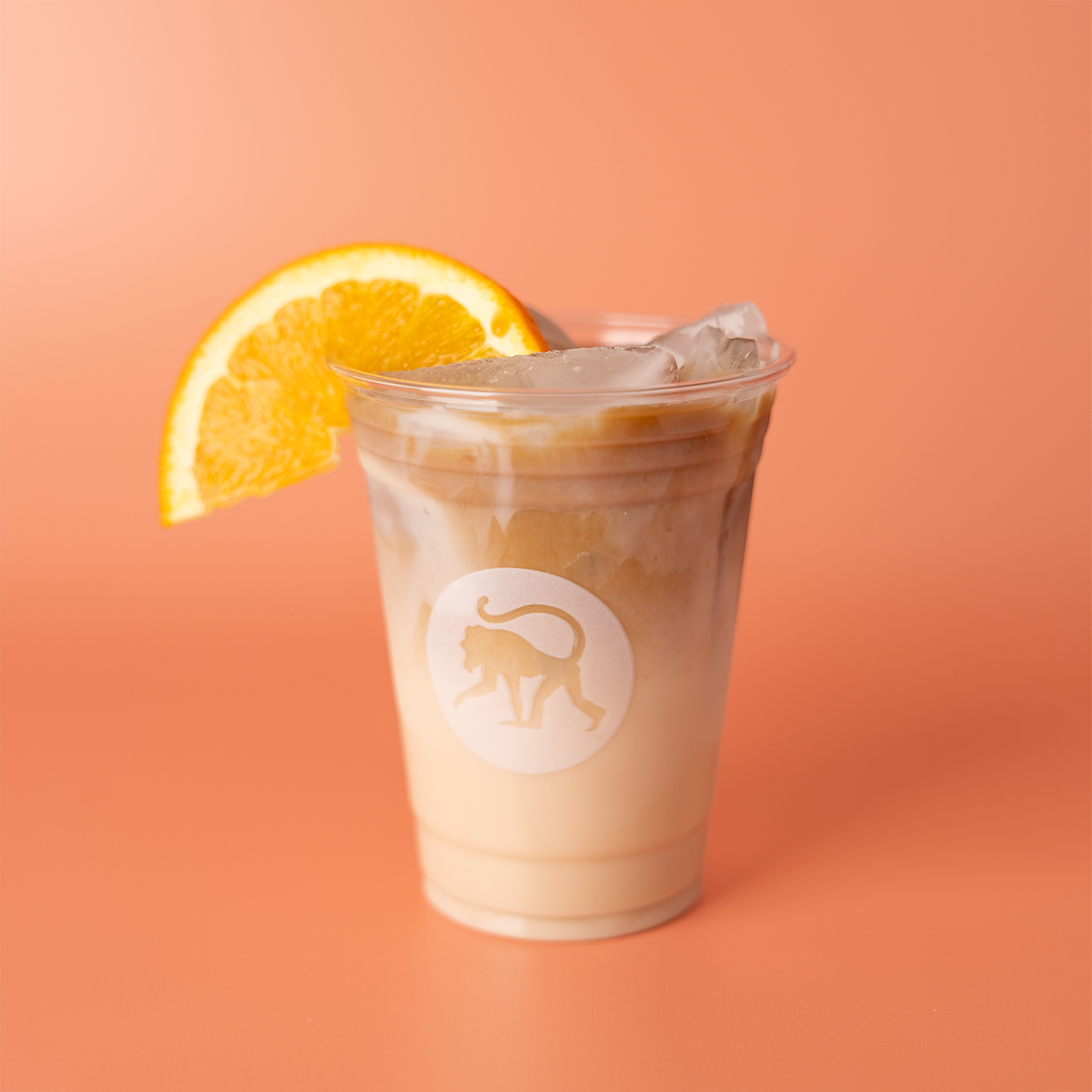 Orange creamsicle cold brew over ice in a Frothy Monkey branded cup, garnished with a fresh orange wedge.