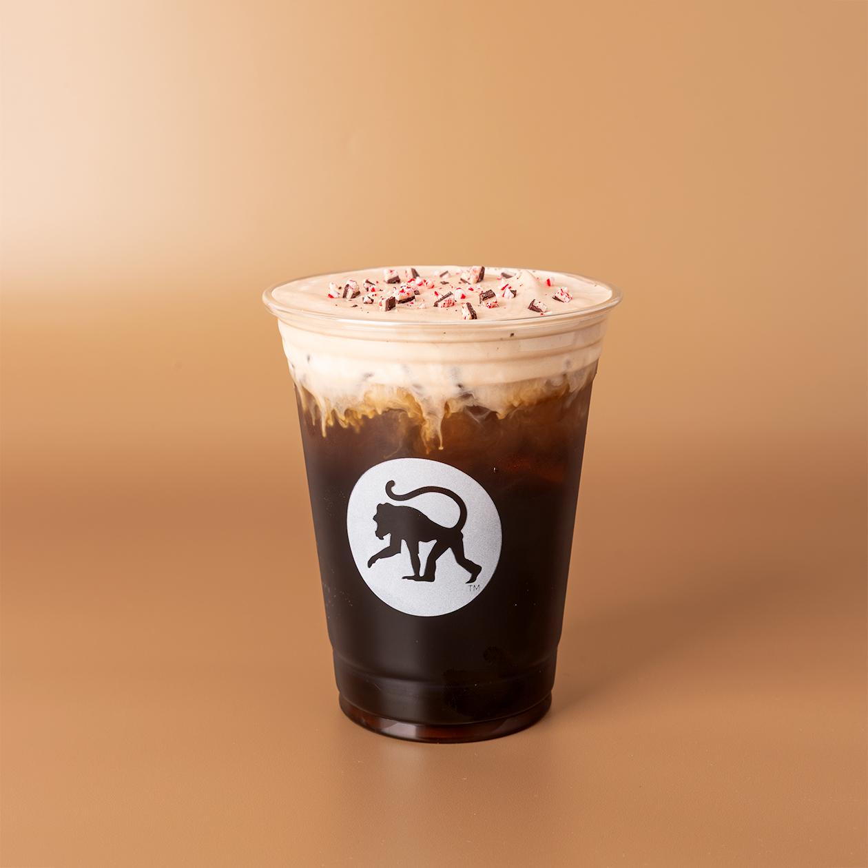 Peppermint bark cold brew in a Frothy Monkey branded cup, topped with cold foam and crushed peppermint candy.