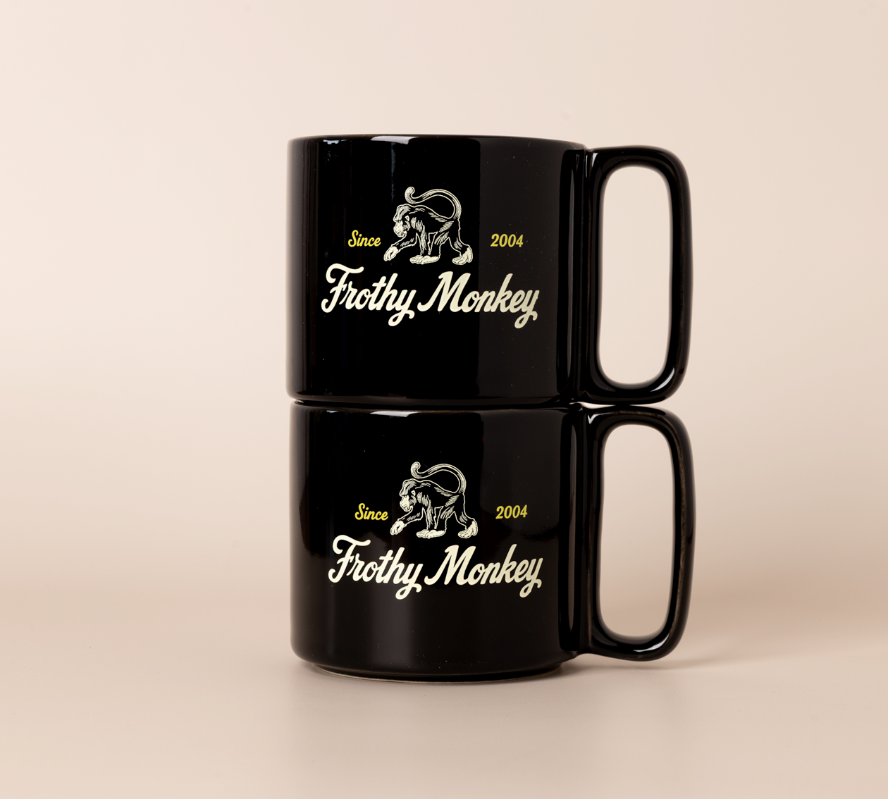 Two Frothy Monkey 10 oz stackable ceramic mugs in Black stacked on top of each other, showing vintage Since 2004 monkey logo in cream with yellow accents