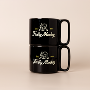 Two Frothy Monkey 10 oz stackable ceramic mugs in Black stacked on top of each other, showing vintage Since 2004 monkey logo in cream with yellow accents