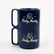 Two Frothy Monkey 10 oz stackable ceramic mugs in Navy Blue stacked on top of each other, showing vintage Since 2004 monkey logo in cream with Howler Blue accents