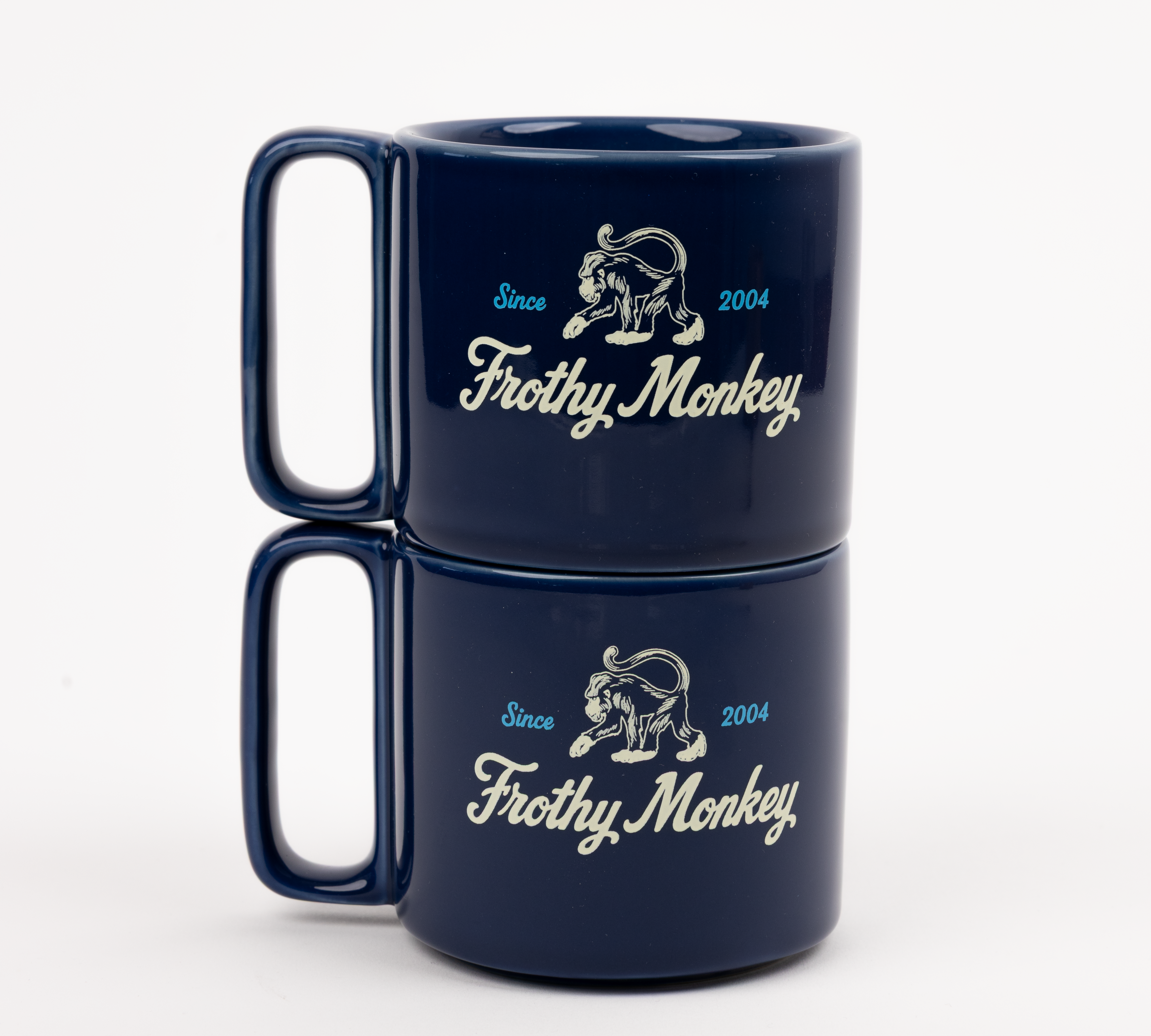 Two Frothy Monkey 10 oz stackable ceramic mugs in Navy Blue stacked on top of each other, showing vintage Since 2004 monkey logo in cream with Howler Blue accents
