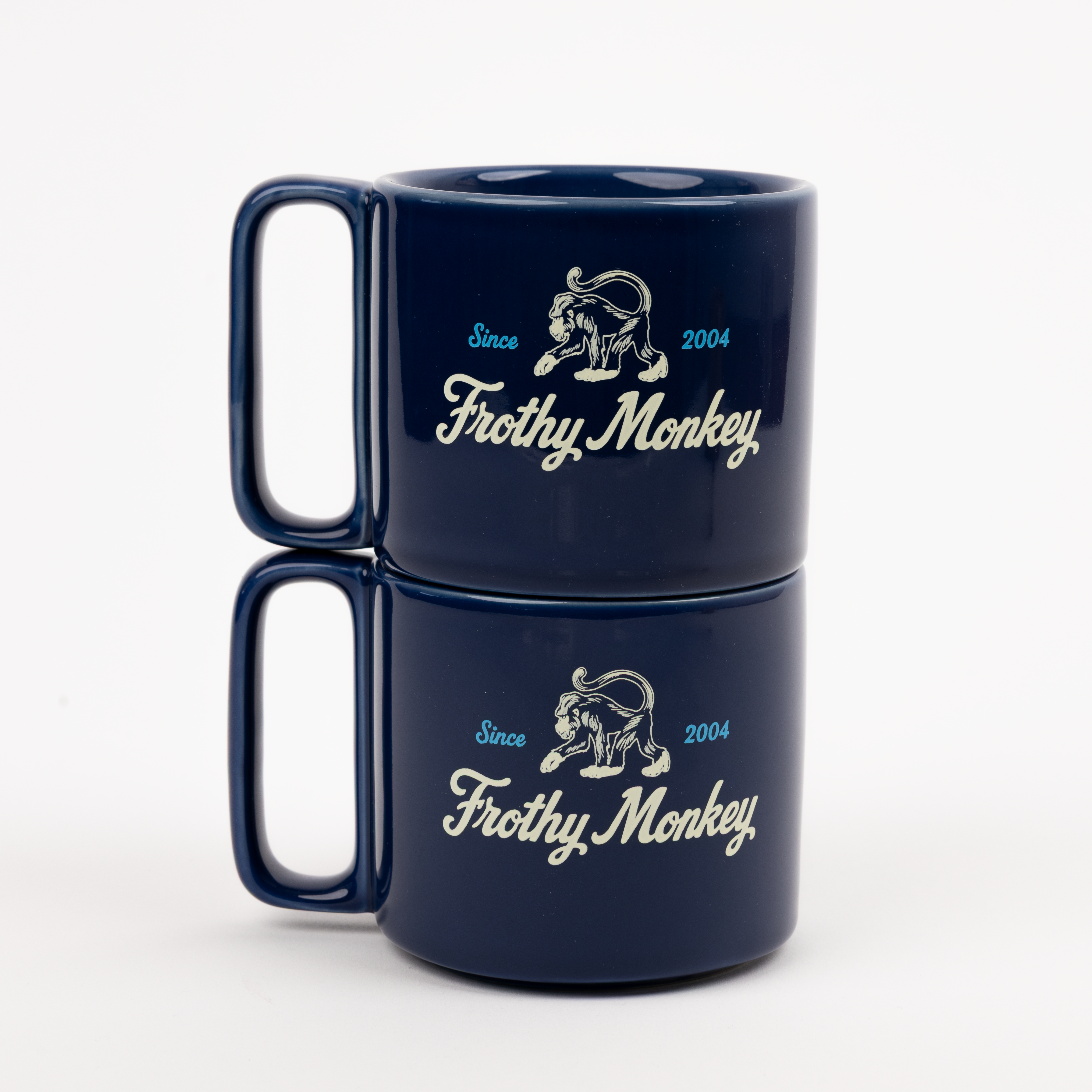 Two Frothy Monkey 10 oz stackable ceramic mugs in Navy Blue stacked on top of each other, showing vintage Since 2004 monkey logo in cream with Howler Blue accents