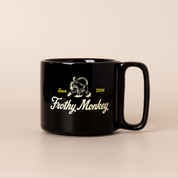Single Frothy Monkey 10 oz stackable ceramic mug in Black with vintage logo in cream and yellow accents, side view