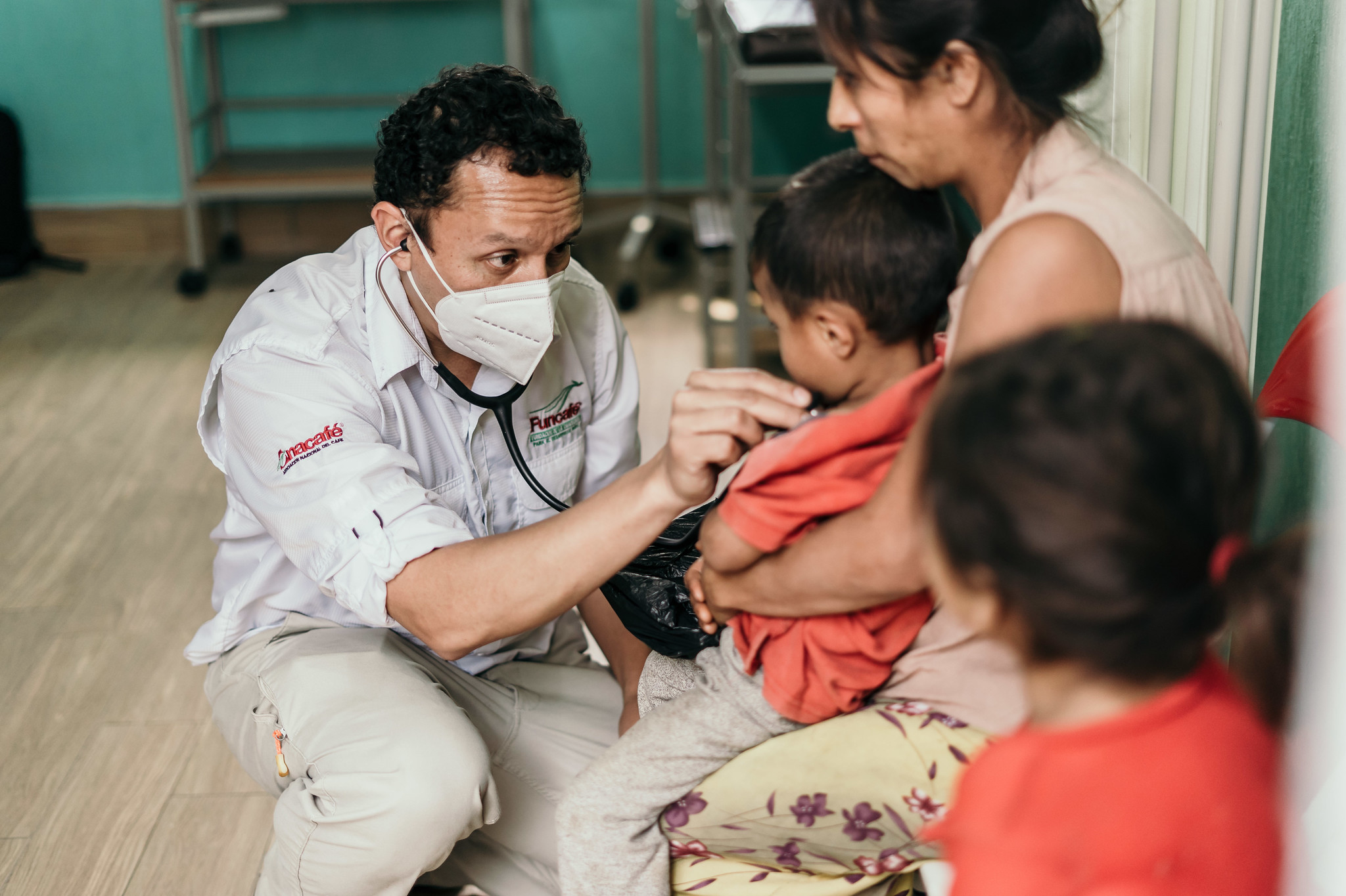 Doctor with a stethoscope examining a young child held by a woman at a health clinic, Guatemala